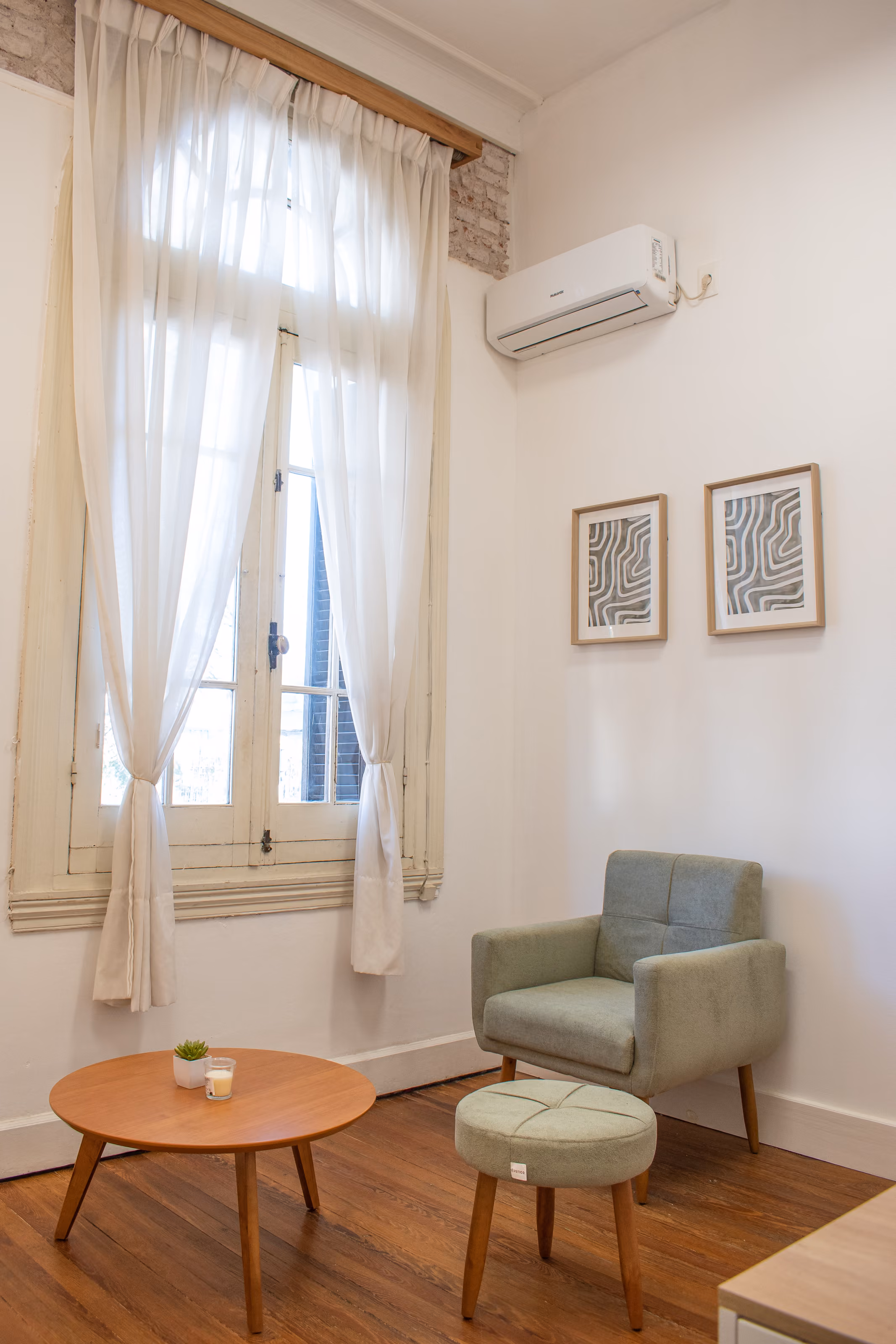 Consultorio 03: la ventana alta con cortinas de voile recogidas, el sillón verde y el puf junto a la mesa baja.